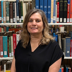 Woman with should length dark blonde hair standing in front of a shelf of books in a library