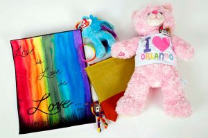Photo of items from the Pulse Memorial Collection: Love is Love flag, My Little Pony beanie baby, gold and red notebook, and a pink "I Heart Orlando" plush bear.
