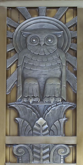Photograph of bas relief metal owl perched on a branch with sun behind 