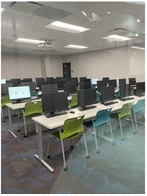 Photo of a classroom featuring blue and green plastic chairs at computer tables.