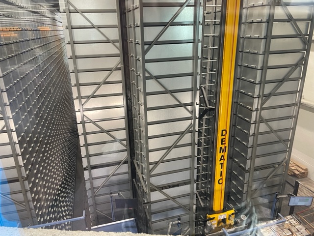 Photograph of the Automatic Retrieval Center which houses silver bins stacked in tall columns which a yellow retrieval unit can locate and bring back for check out.