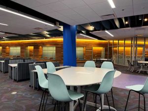 Photo of the third floor seating options of the John C Hitt Library featuring a white table in teh foreground surrounded by sea green plastic chairs.