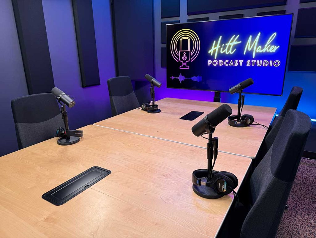Hitt Maker recording area showing 4 chairs and microphones around a table with a large monitor