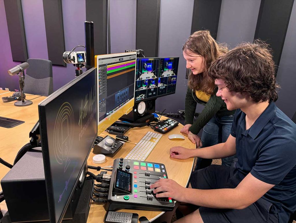 Two students using the podcast studio engineering equipment to control a podcast recording.