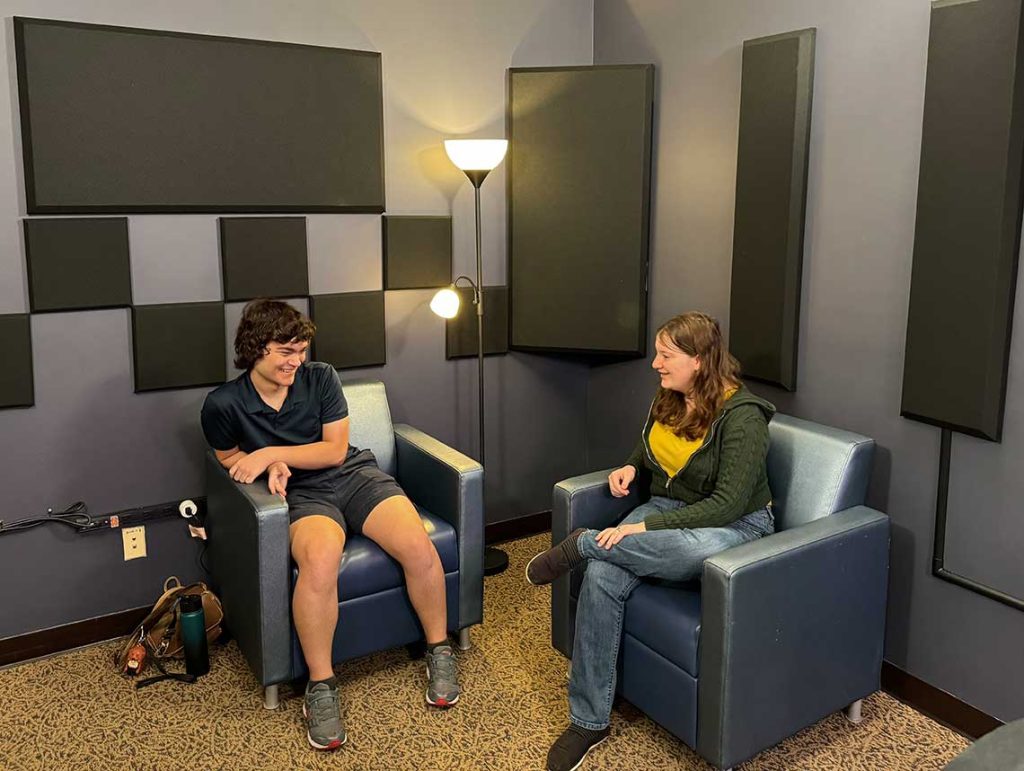 Two students in comfy chairs in the corner of the Hitt Maker Podcast Studio