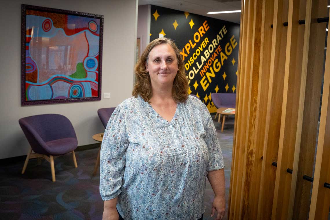 Woman standing confidently in a modern workspace, showcasing vibrant art and welcoming decor.