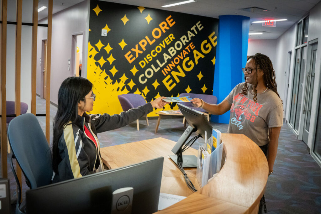 A student assistant sitting at a help desk helping another student with a problem.