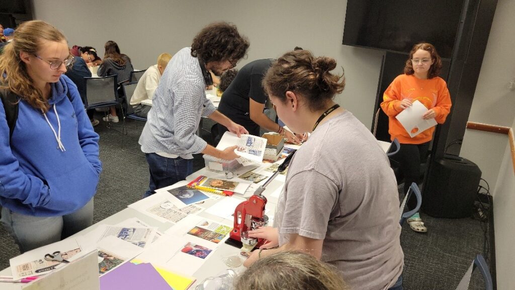 Students stand around a table making pinback buttons using markers, scissors, and paper copies of images from the Robert H. Brown tourism collection. Student intern, Sofia, operates the button-making machine.