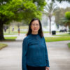 Woman standing outside at University of Central Florida campus with trees and a fountain in the background.