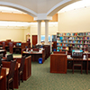 Image of the inside of a Library with chair, book shelves and computers.