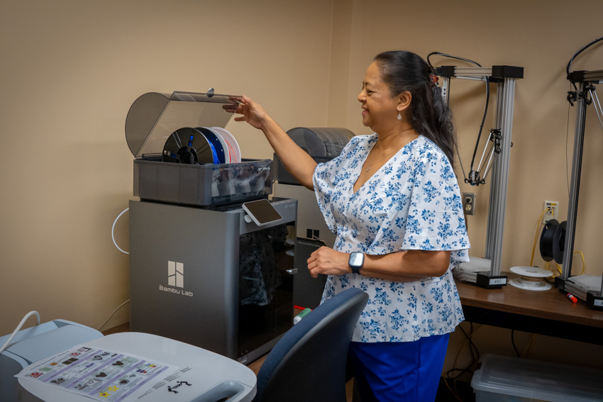 Woman standing next to 3D printer opening it up and getting ready to use it.