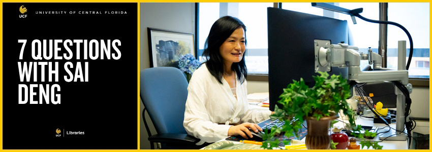 Woman with black hair sitting a desk with a computer in front of her as she works.