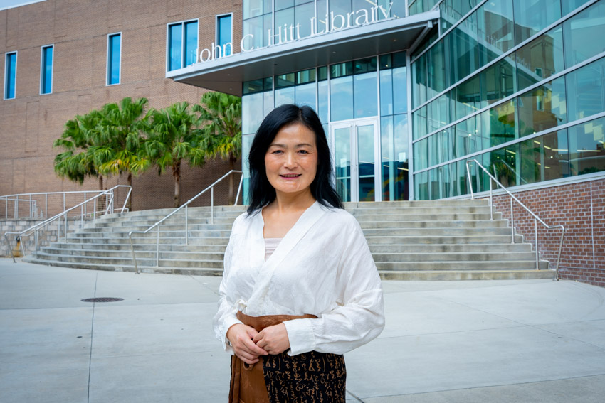 Woman with black hair standing outside of a library with stairs in the background.