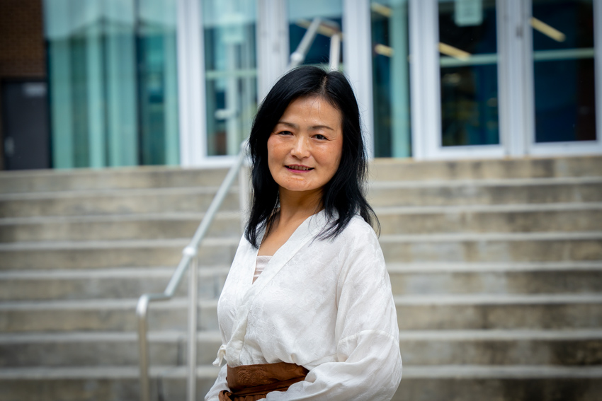 Woman with black hair standing outside of a library with stairs in the background.