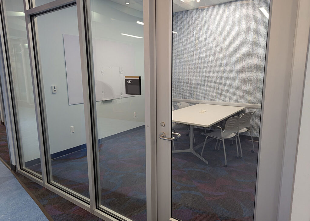 Study room with a rectangular table and four chairs on caster wheels with whiteboard mounted on the wall.