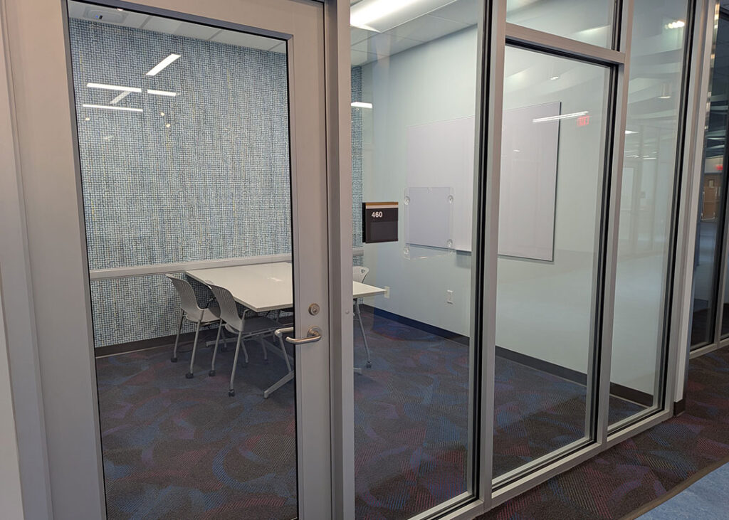 Study room with a rectangular table and four chairs on caster wheels with whiteboard mounted on the wall.
