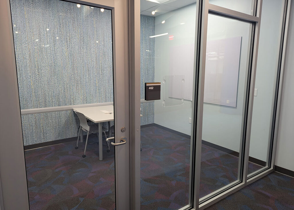 Study room with a rectangular table and two chairs on caster wheels with whiteboard mounted on the wall.