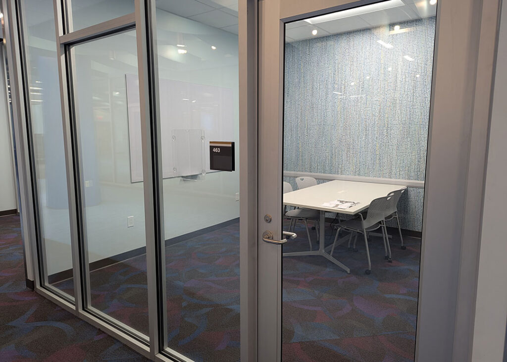 Study room with a rectangular table and four chairs on caster wheels with whiteboard mounted on the wall.