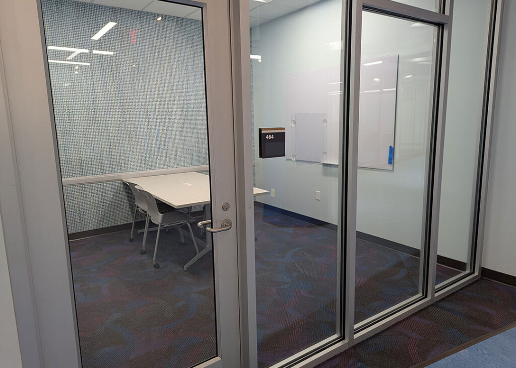 Study room with a rectangular table and four chairs on caster wheels with whiteboard mounted on the wall.