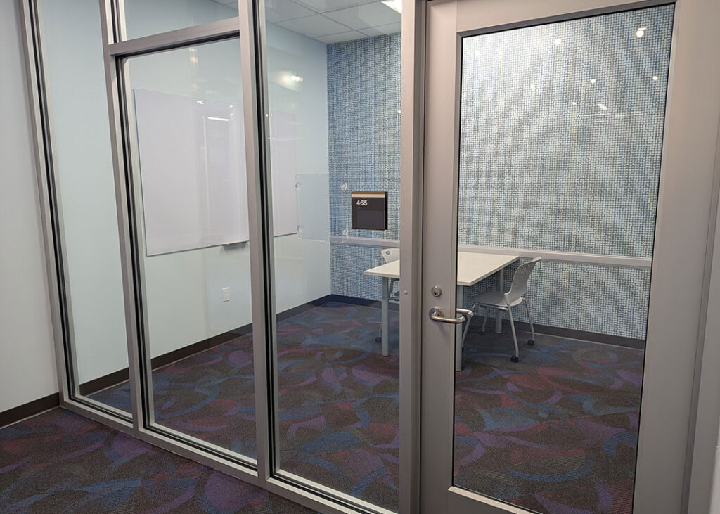 Study room with a rectangular table and two chairs on caster wheels with whiteboard mounted on the wall.