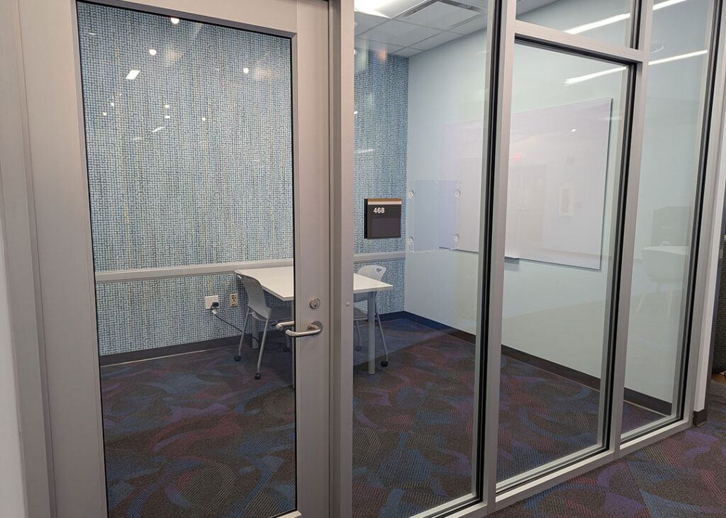 Study room with a rectangular table and four chairs on caster wheels with whiteboard mounted on the wall.