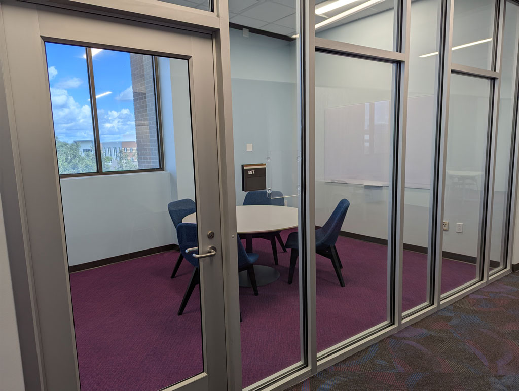 Study room with a small rounded table and four softer chairs with a whiteboard mounted on the wall. Also has a window.
