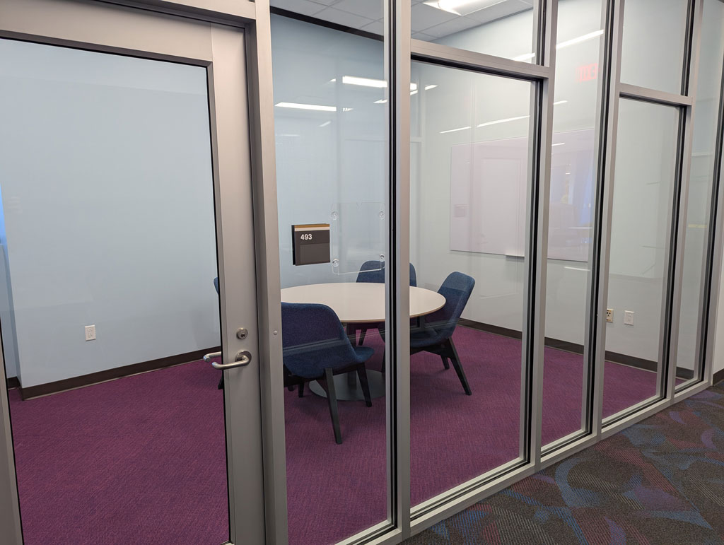 Study room with a small rounded table and four softer chairs with a whiteboard mounted on the wall. Also has a window.