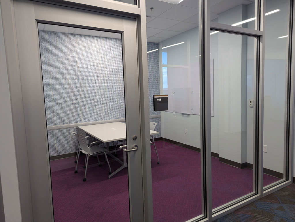 Study room with a rectangular table and four chairs on caster wheels with whiteboard mounted on the wall.