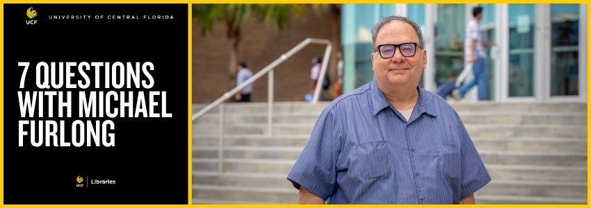 Man standing outside of a brick building with glasses on and a blue striped shirt