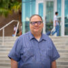 Man standing outside of a brick building with glasses on and a blue striped shirt