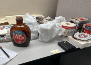 Table with various items commemorating the 1976 U.S. Bicentennial, including a Log Cabin Syrup bottle, Marcal toilet paper roll, frisbee, napkins, glass mugs wrapped in tissue paper, and a Liberty Bell box.