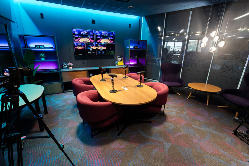 podcast studio with colorful lighting, comfortable chairs around a table with microphones