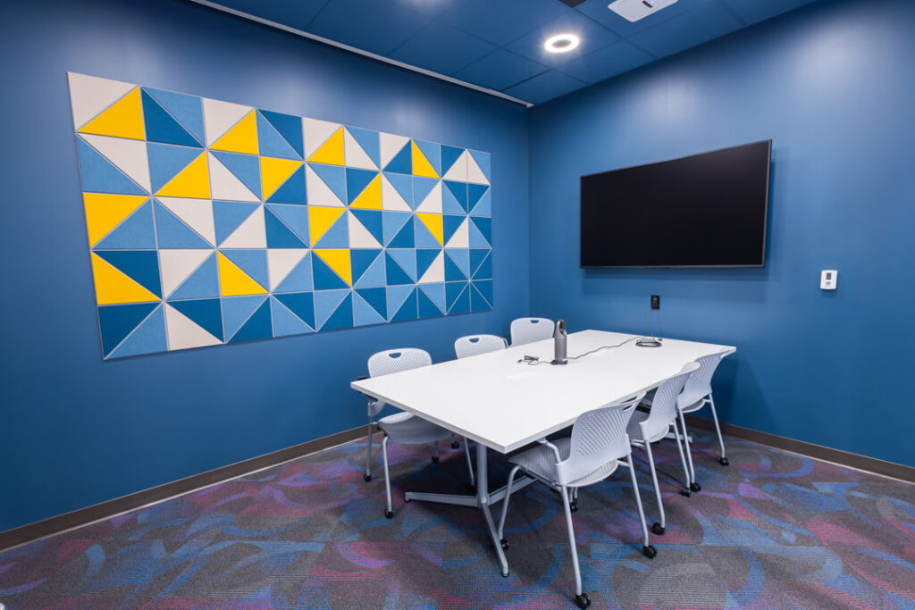 Six person conference room with a table and chairs with a wall mounted monitor.