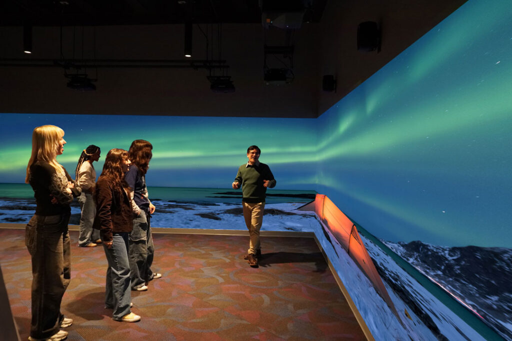 Room with 3 wall wrapped image projection with people viewing the projectors