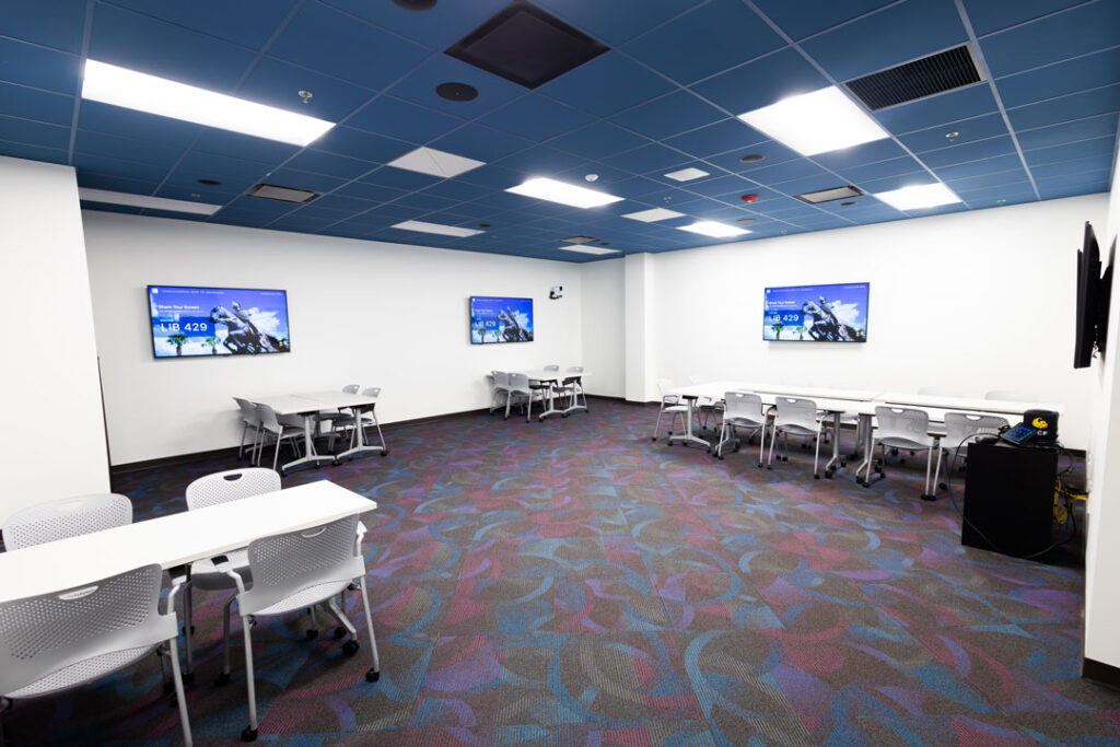 Open instruction room with wall mounted monitors, tables, and chairs.