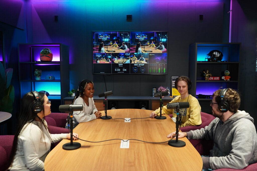 students sit around a table with microphones recording a podcast
