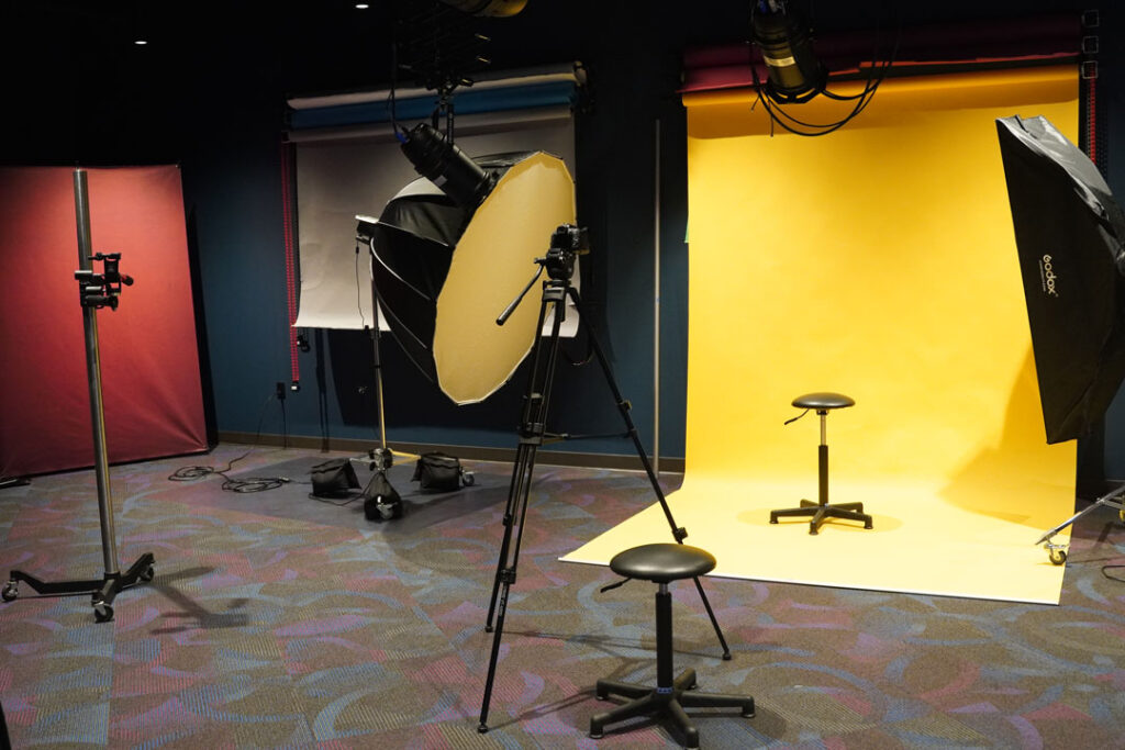 Large room filled with photogrophy equipment including, lights, tripods, backdrops, and stools.
