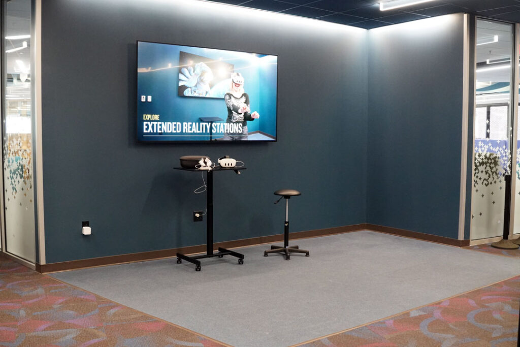 Open space used for Extended Reality, including Virtual Reality headsets. Has a monitor on the wall and a table with a VR headset.